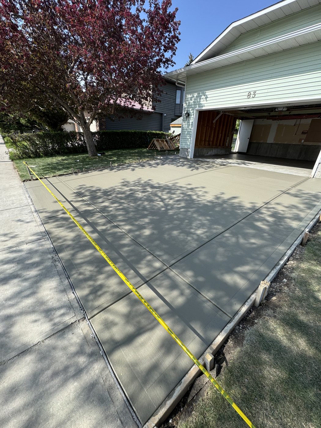 Freshly poured brushed concrete driveway replacement at a Citadel home in NW Calgary by Patriarch Construction, control joints cut and curing