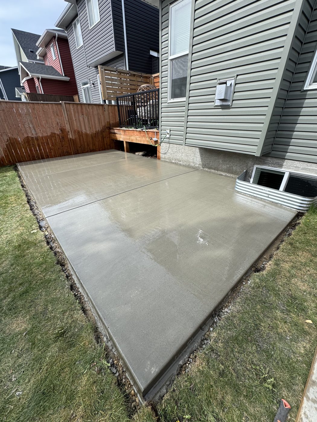 New brushed concrete backyard patio poured in Citadel, Calgary, with cut control joints and a clean edge against the lawn