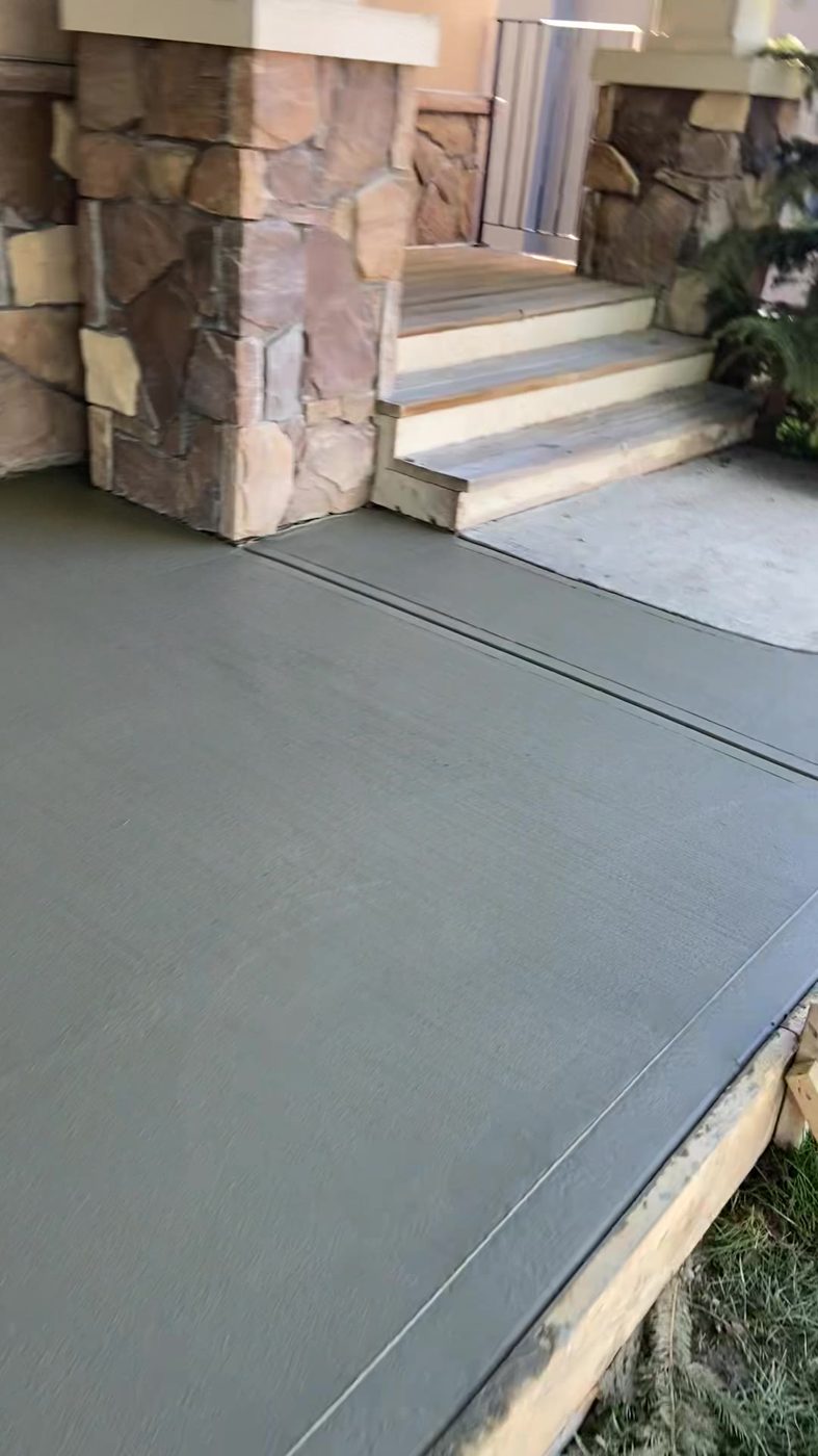Freshly poured brushed concrete front-entry walkway with a tooled control joint leading to stone-clad steps on a new-build home in Redstone, NE Calgary by Patriarch Construction