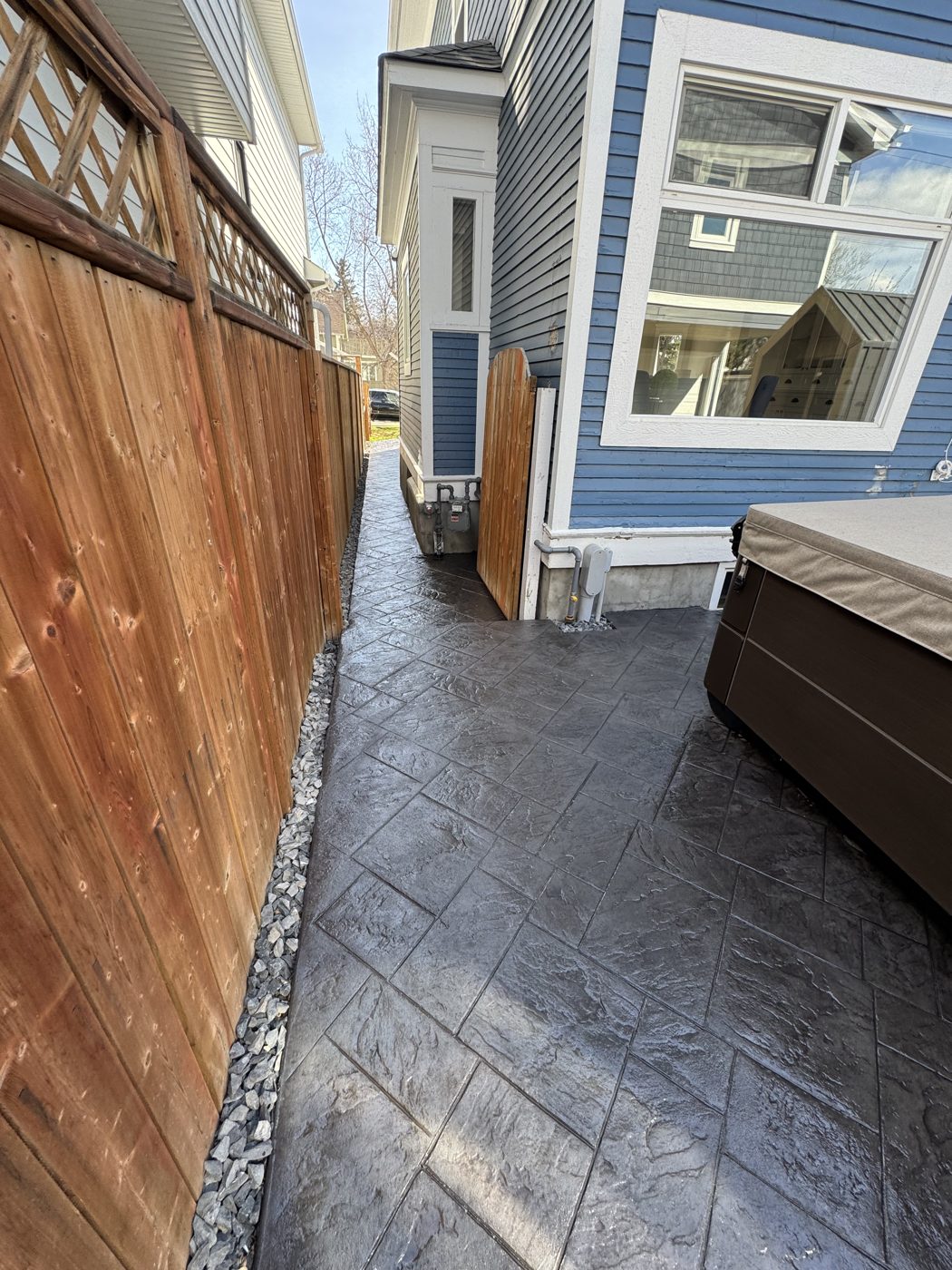 Slate-pattern stamped concrete side-yard walkway poured beside a Royal Oak home in NW Calgary by Patriarch Construction, with a gravel drainage strip