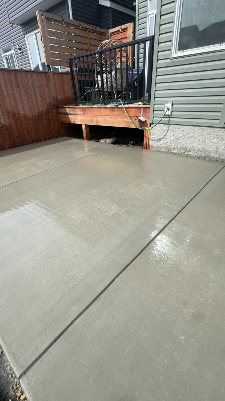 Freshly poured brushed concrete backyard patio under a raised deck on a walkout lot in Tuscany, Calgary by Patriarch Construction