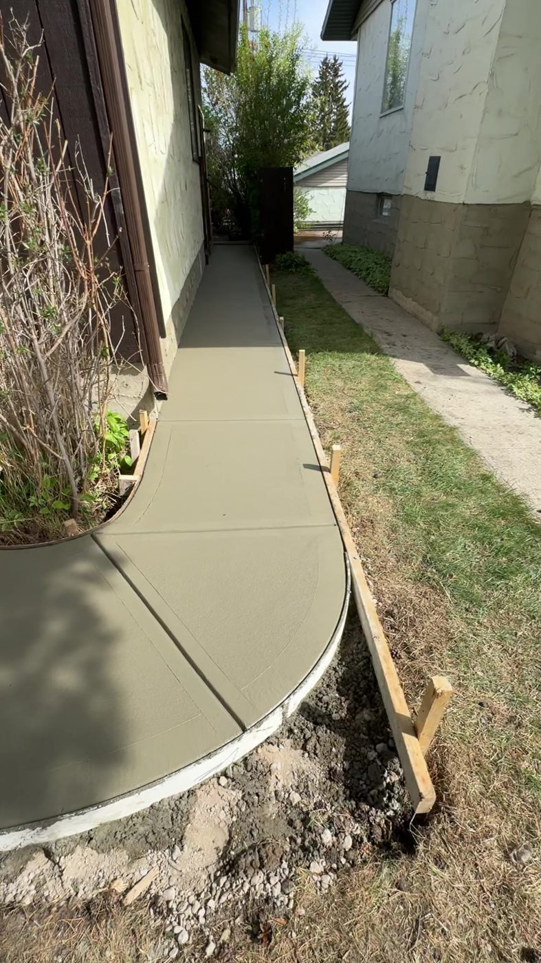 Curved brushed concrete side walkway poured with forms in place beside a Tuscany home in NW Calgary by Patriarch Construction
