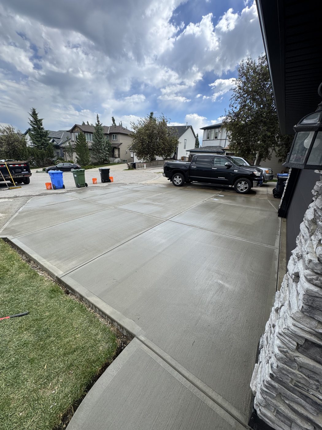 New brushed concrete driveway poured beside a stone-clad West Springs home in SW Calgary by Patriarch Construction, curing in the sun